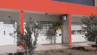 Frente del complejo Pewmafe en Las Grutas: departamentos de planta baja con galería y olivos en el jardín